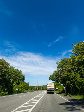 A truck driving down a road with trees on both sides of it.の写真素材