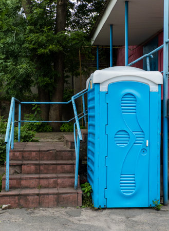 Blue portable toilet standing on the side of the building.の写真素材