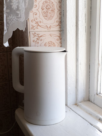 A white kettle sitting on a window sill next to a window.の写真素材