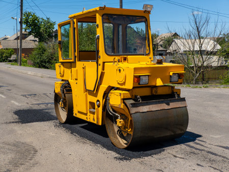 A large yellow road roller sitting on the side of a road.の写真素材