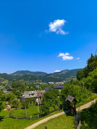 View of the mountains and herbaceous field with a fence and a small house at a distance.の写真素材