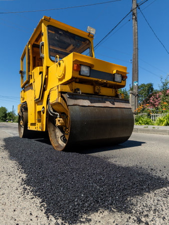 A large yellow road roller on the side of a road.の写真素材