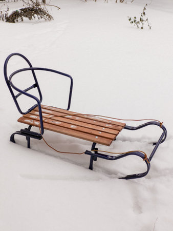 A classic wooden sled with a dark blue metal frame rests on a thick blanket of fresh snow. The...