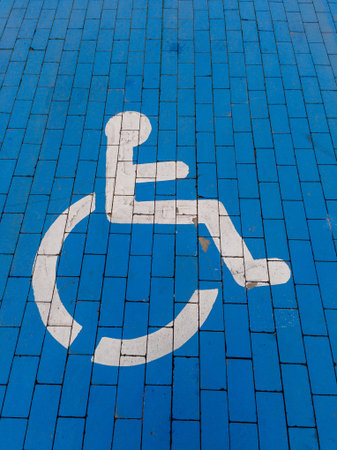 Close-up of a white wheelchair accessibility symbol painted on a vibrant blue tiled surface. This...