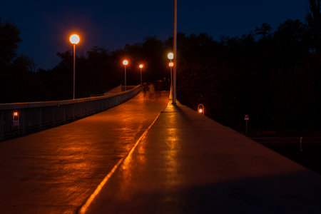 Dark pedestrian bridge lit up by street lights over rowing canalの写真素材
