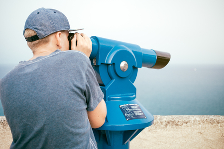 Teenager is looking through panoramic telescope. Young man observing the landscape. Watching the sightseeingsの写真素材