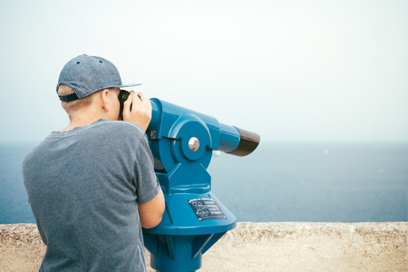 Teenager is looking through panoramic telescope. Observing the landscape.の写真素材