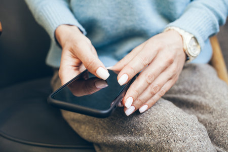 Close-up of woman hands with beautiful manicure and white nail polish holding smart phone and using...