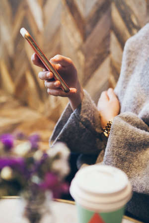 Close-up of woman's hands holding cell phone while drinking coffee from take away paper cup. Lifestyle, reading news, social network, surfing the web / internet in smartphone. Coffee break business.の写真素材