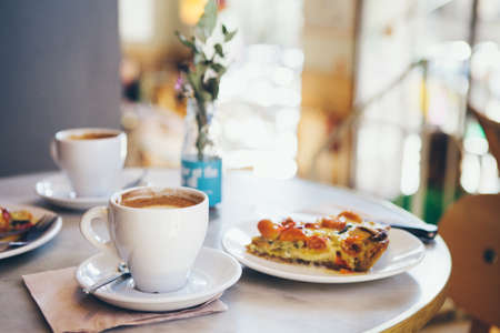 Close-up of a breakfast for two persons in a nice cafe, warm quiche and coffee, no people blurry background. Film effect.の写真素材