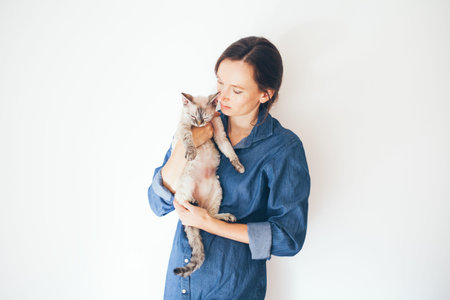 Happy young woman with her Devon Rex cat. Young woman is holding and hugging her cute curious Devon...