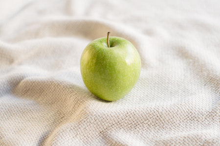 Close-up of single green juicy apple on the table with white tablecloth. Food photography using natural window light. Eating green apples helps increasing the body's metabolism.の写真素材