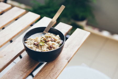 Black color plate with home made porridge and pistachios on the wooden outdoor table on the apartment balcony. No people, healthy eating breakfast concept. Selective focus, natural light photoの写真素材