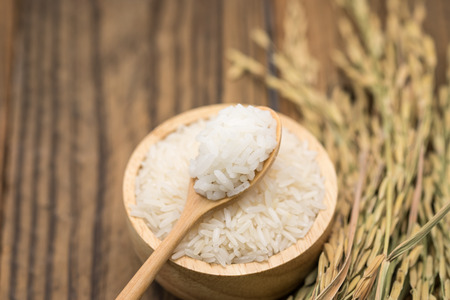 Jasmine rice grains in wooden bowl with dry leafの写真素材