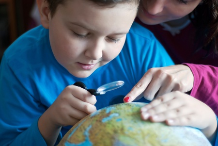 Concentrated boy sitting and searching something at globe with his motherのeditorial素材