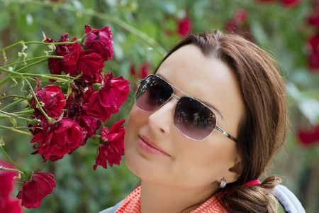 Beautiful young brunette in garden under red roses bower.の写真素材