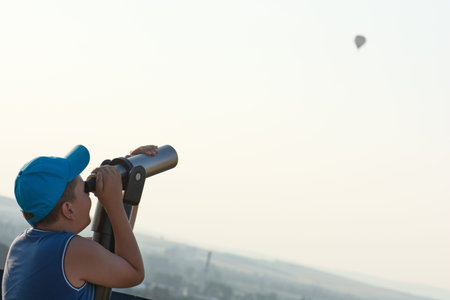The little boy watching the flying baloon through telescope.