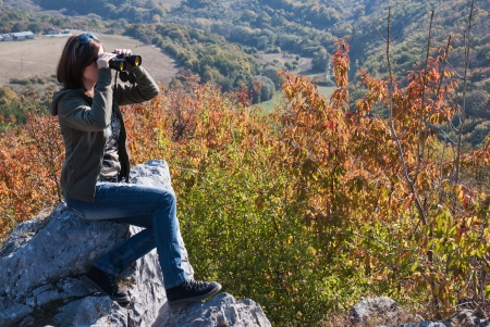 Beautiful woman with binoculars watching autumn nature.の写真素材