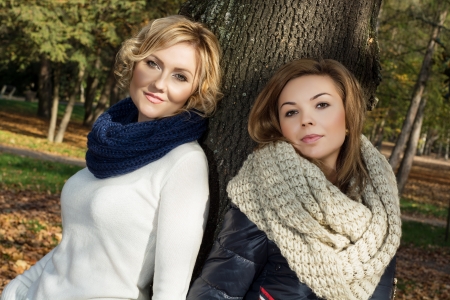 Two beautiful young women posing in front of a tree in autumn park.の写真素材