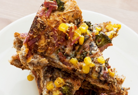 Slices of tasty pizza with corn, ham, cheese, broccoli and mushrooms.の写真素材