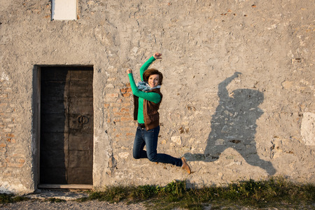 Young caucasian woman is jumping for joy in front of the old wall.の写真素材