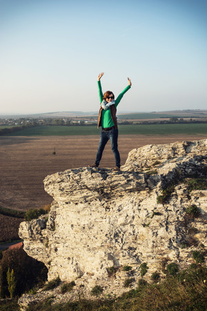 Young caucasian joyful woman posing on the high rock at sunset.の写真素材