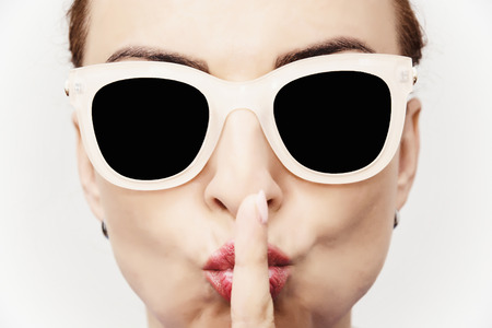 Young caucasian glamour woman with stylish sunglasses and finger to her mouth. Beauty and fashion.の写真素材