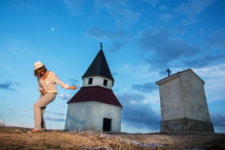 Young caucasian woman imitates guitar playing by the church on the hill.の写真素材