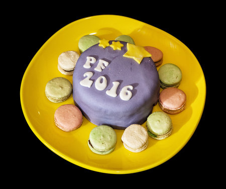 The title PF 2016 written on festive cake with handmade macaroons on yellow plate.