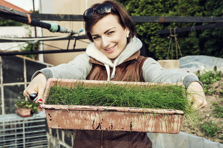 Joyful caucasian young woman with pot of chive in the garden. Seasonal gardening theme. Gardener woman posing with plant. Outdoor female portrait. House and garden.の写真素材