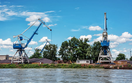 Blue cranes in cargo port translating coal. Industrial scene. Big port-cranes. Danube river.