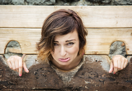 Young caucasian woman in medieval pillory. Negative emotions. Misery theme. Punishment device.の写真素材