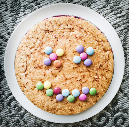 Tasty cake with colorful smarties in funny face shape. Festive sweet food. Positive emotions.