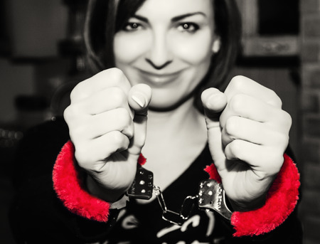 Young caucasian woman posing with red handcuffs at the party. Sexy female portrait. Crime theme. Submissive role.の写真素材