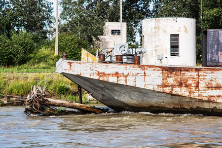 Old rusty anchored boat by riverside. Industrial scene.の写真素材