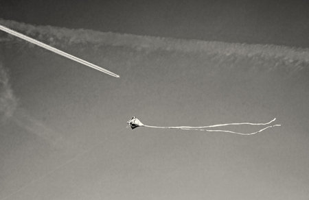 Flying colorful kite and airplane on the sky. Black and white photo.