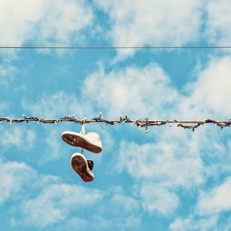 Sneakers hanging on the power line. Blue sky. Bad joke. Beauty photo filter.の写真素材