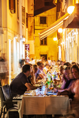 POREC, CROATIA â AUGUST 10, 2018: Tourists are sitting in the garden restaurant, old town of Porec, Croatia. Evening time in summer vacation destination. Illustrative editorial.のeditorial素材