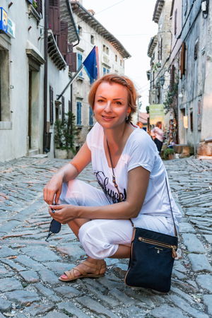 GROZNJAN, CROATIA: Young touristic woman posing in stoned street in Groznjan, Istria, Croatia. Sunset scene. Travel destination. Illustrative editorial.の写真素材
