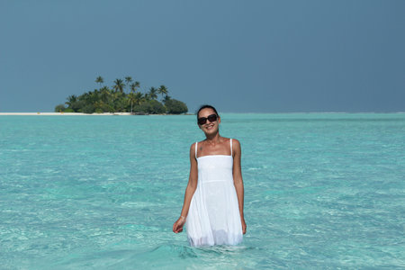 young women in a white dress standing in the water near the Maldive Islandsの写真素材