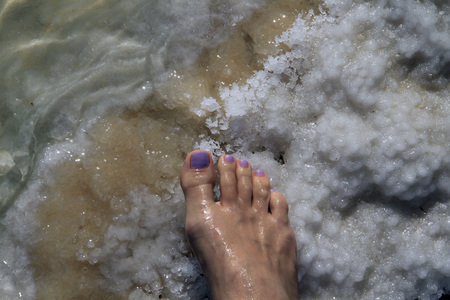 Female foot with pedicure stands on Dead Sea saltの写真素材