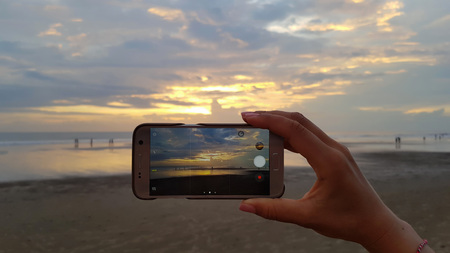 Female hand takes off on your smartphone sunset on the oceanの写真素材