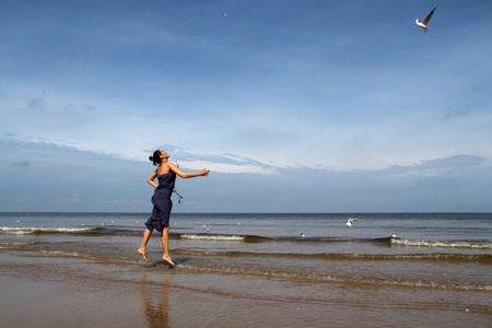 Baltic sea,   woman  in summer dress  feeding white gulls in beachの写真素材