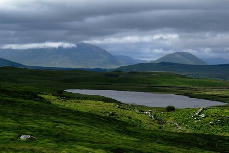 Irish summer landscape, green fields, mountain lake, stormy clouds, distant mountains from Connemara, Galway, Irelandの写真素材