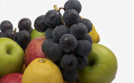 A pile of fresh fruit including red and green apples, lemons,and grapes with plenty of white spaceの写真素材
