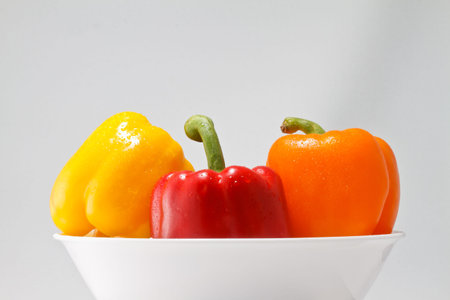 Colorful Yellow Red and Orange Bell Peppers in a White Bowl on a Light Background