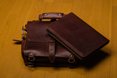 Brown worn leather briefcase and portfoilia on a hardwood floorの写真素材