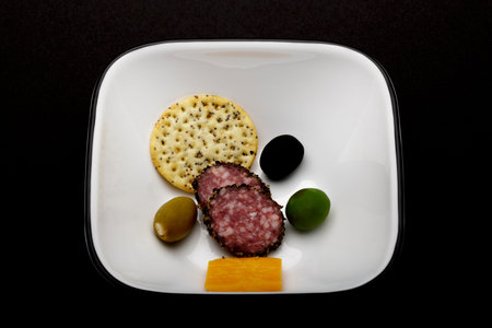 selection of cheddar cheesepeppered hard salami a sesame cracker and three colorful olives