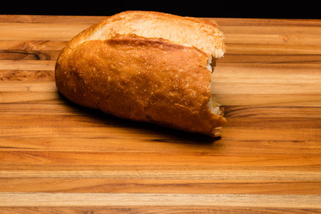 Half a loaf of Italian bread with the heel torn off on a teak wood cutting board