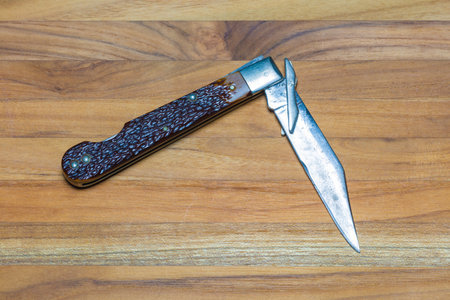 A worn and pitted folding knife against a wood background